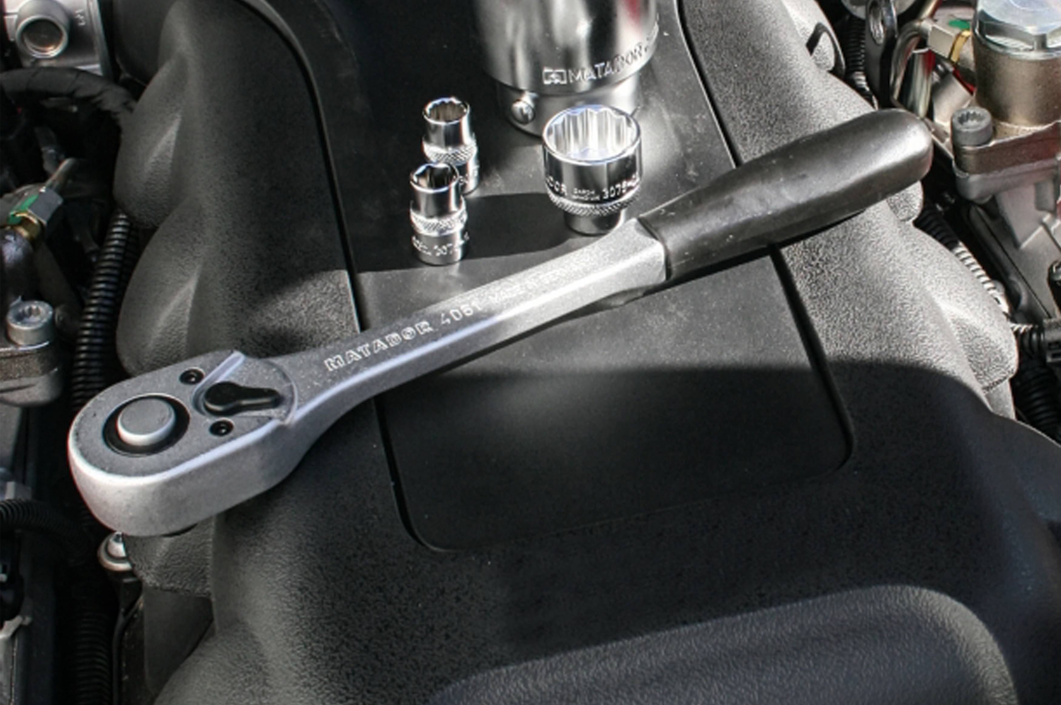 Klucz nastawny leży na części silnika. W tle widać kilka nasadek stojących na bloku silnikowym.