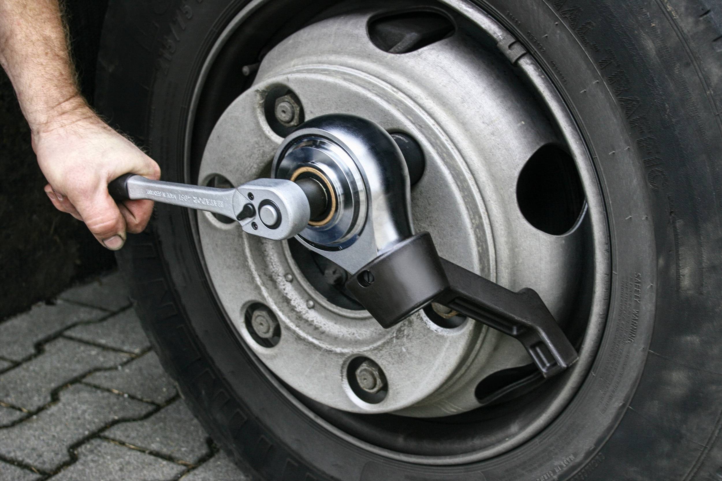 Osoba mocuje nakrętki koła samochodu kluczem dynamometrycznym na utwardzonej nawierzchni.