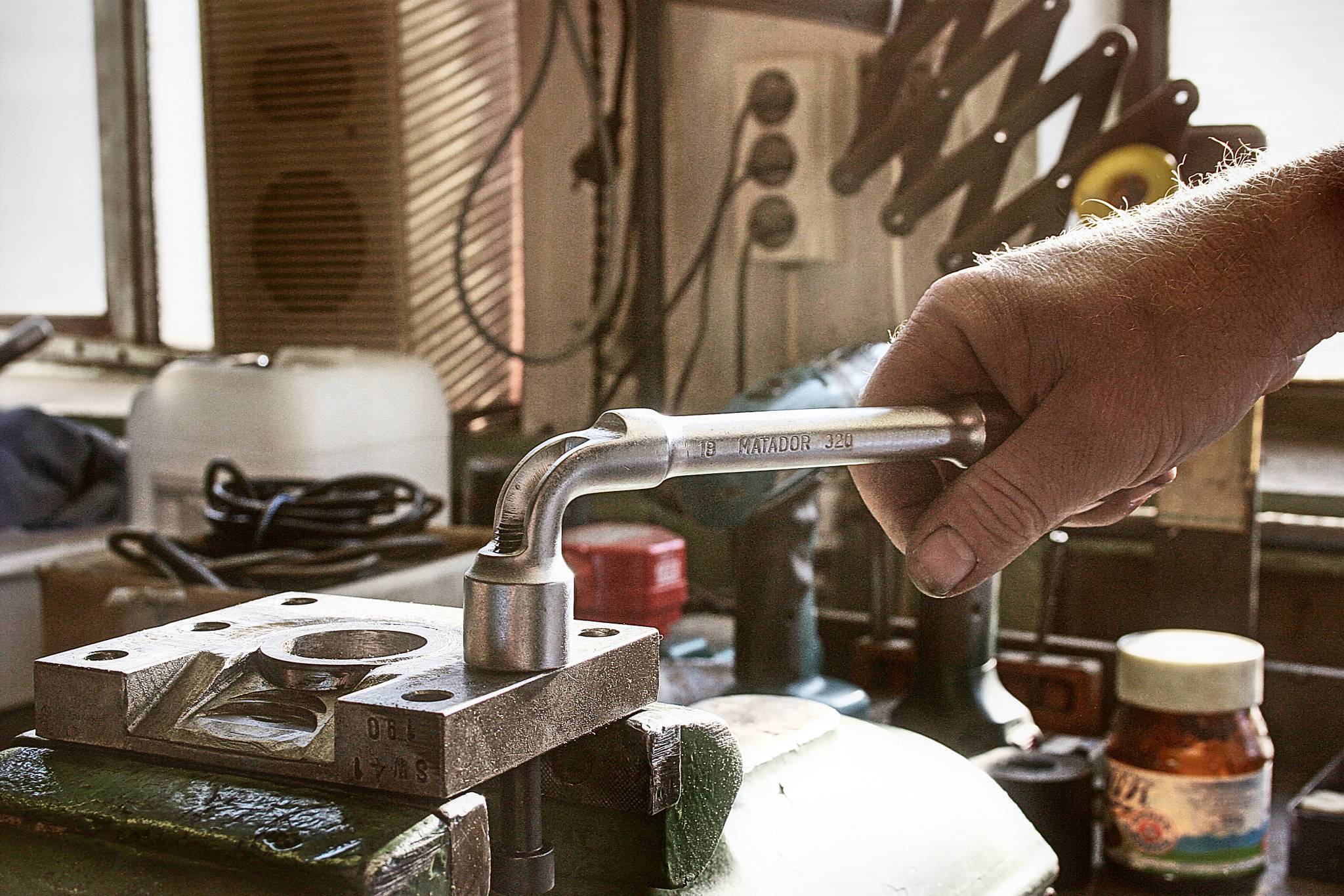 Osoba używa klucza do dokręcenia metalowej płyty w środowisku warsztatu.