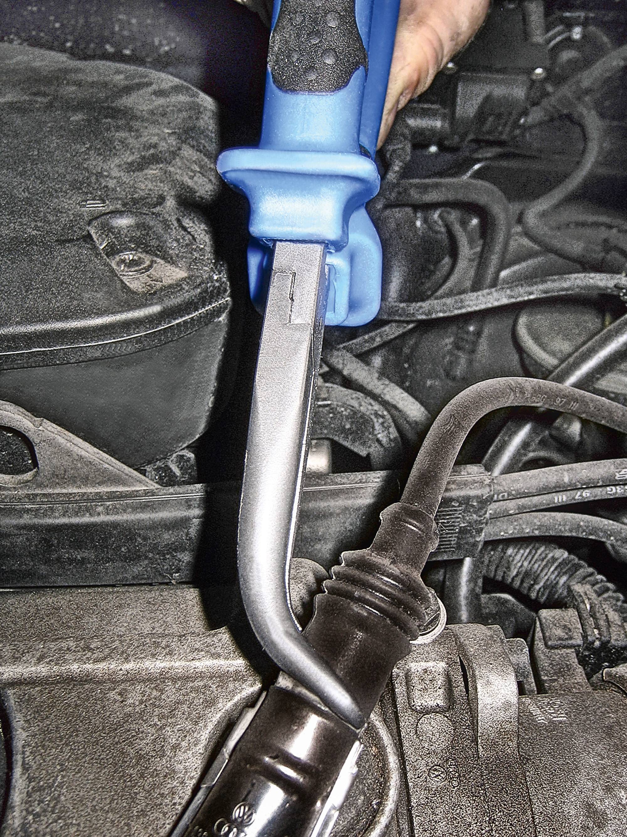 Ręka używa niebieskiego specjalistycznego narzędzia do odkręcania cewki zapłonowej w samochodzie. Widoczne są kable i części silnika.