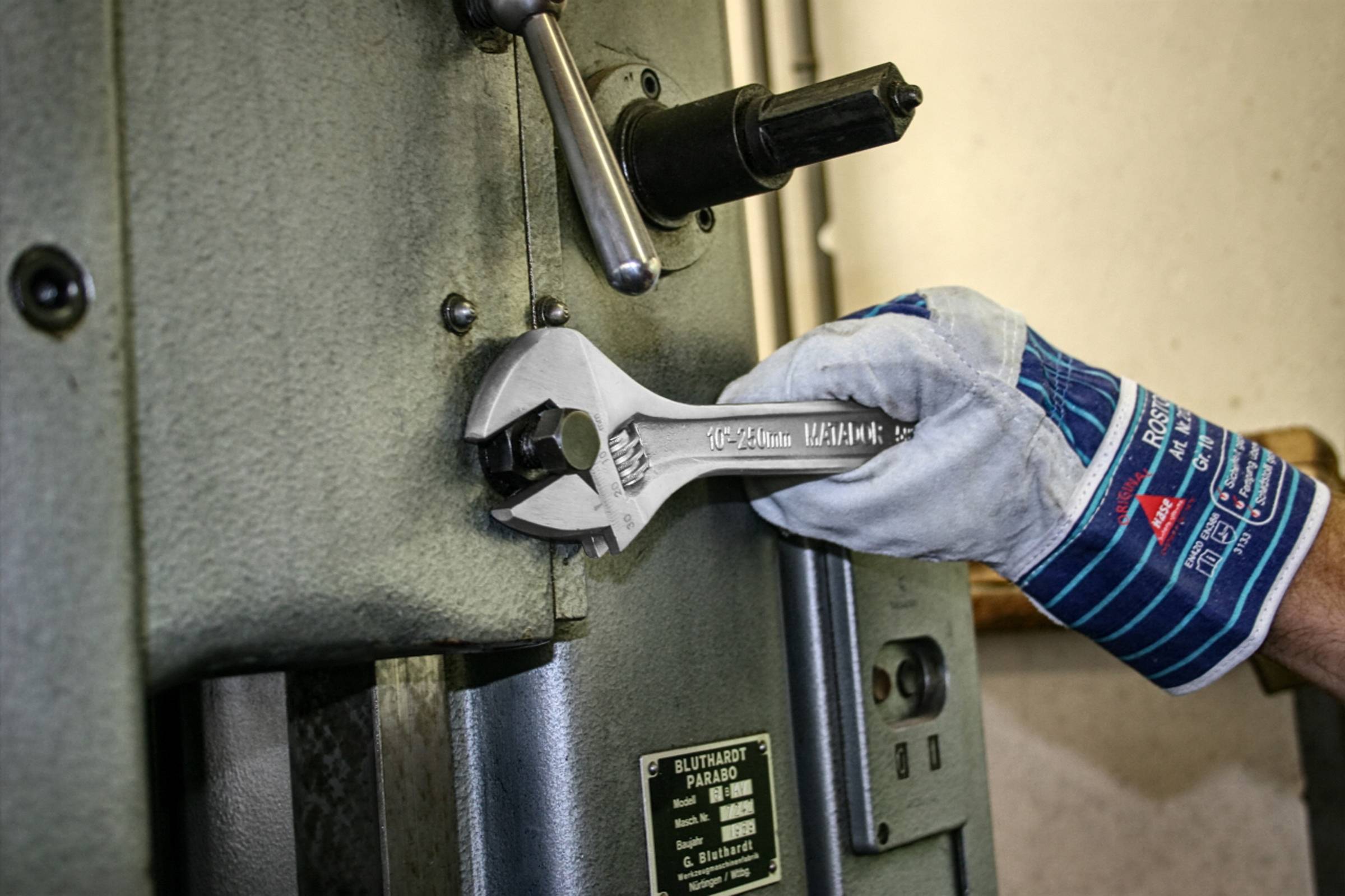 Osoba w rękawicach dokręca śruby przy dużej metalowej maszynie za pomocą klucza.