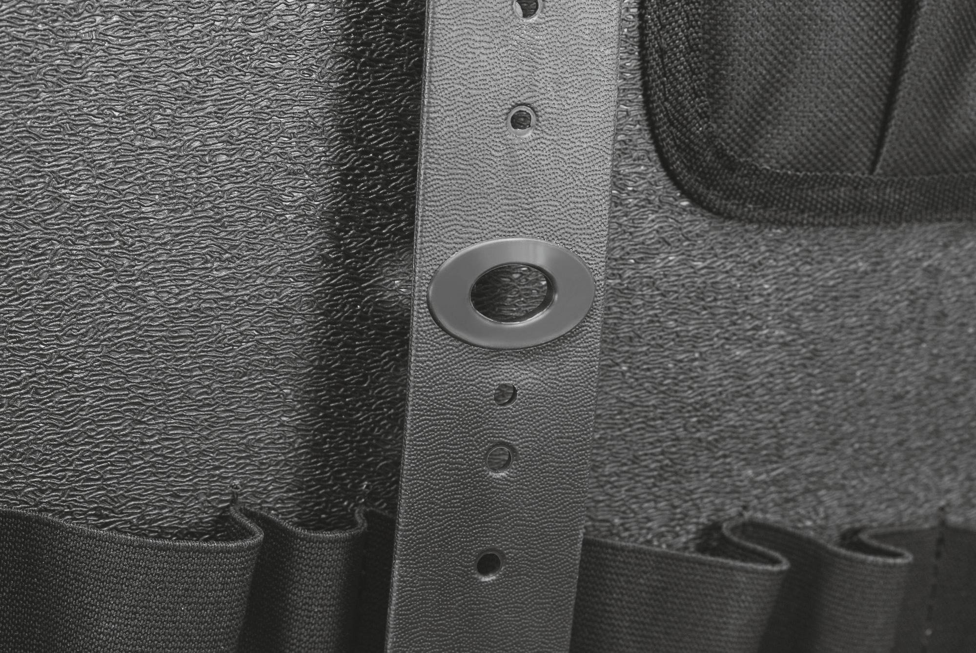 Zbliżenie pasa w kolorze czarnym z wieloma otworami, leżącego na strukturyzowanej, szarej powierzchni.