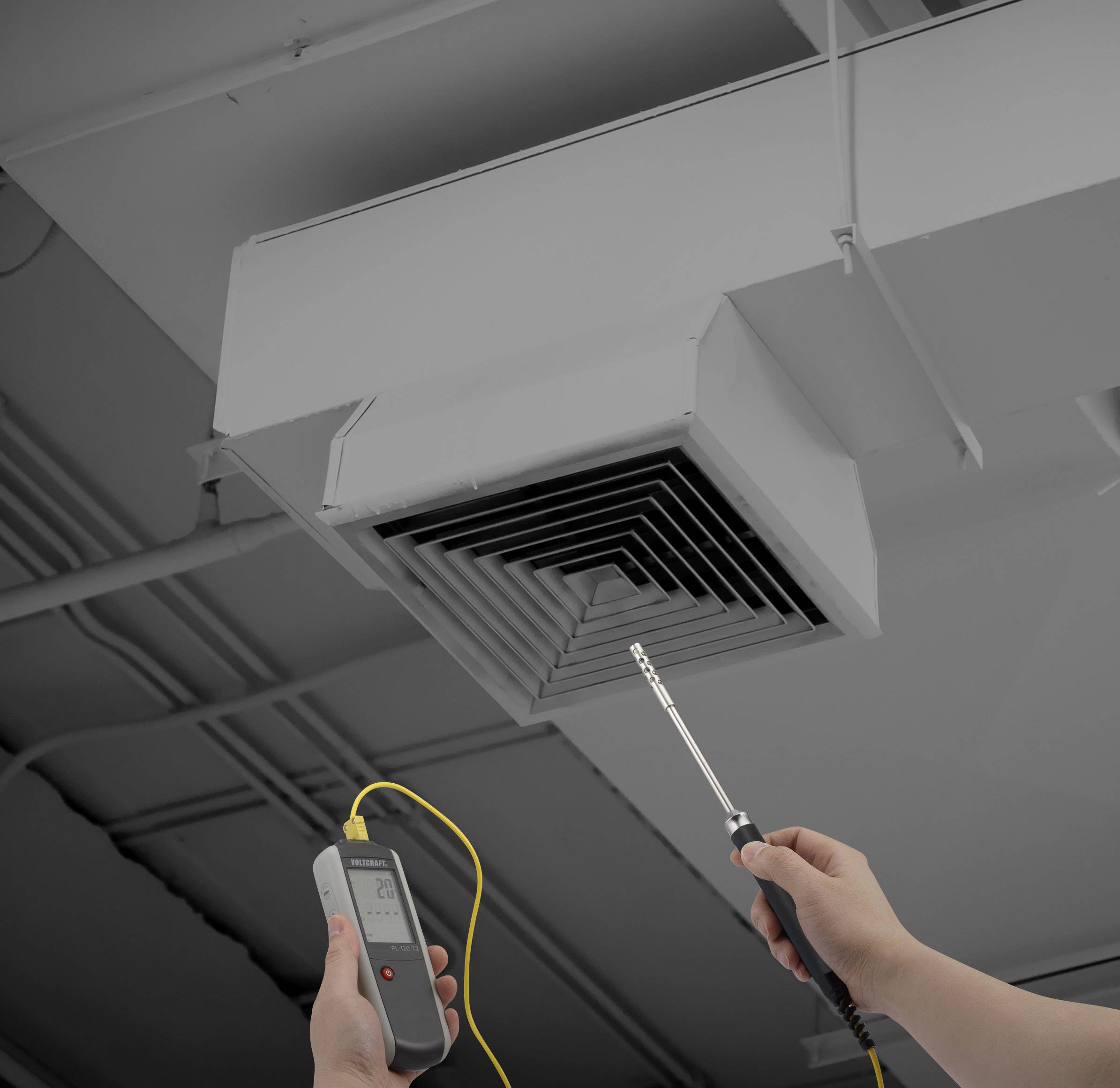 Osoba trzyma urządzenie pomiarowe przed wylotem wentylacyjnym na suficie, aby sprawdzić przepływ powietrza lub efektywność temperaturową.