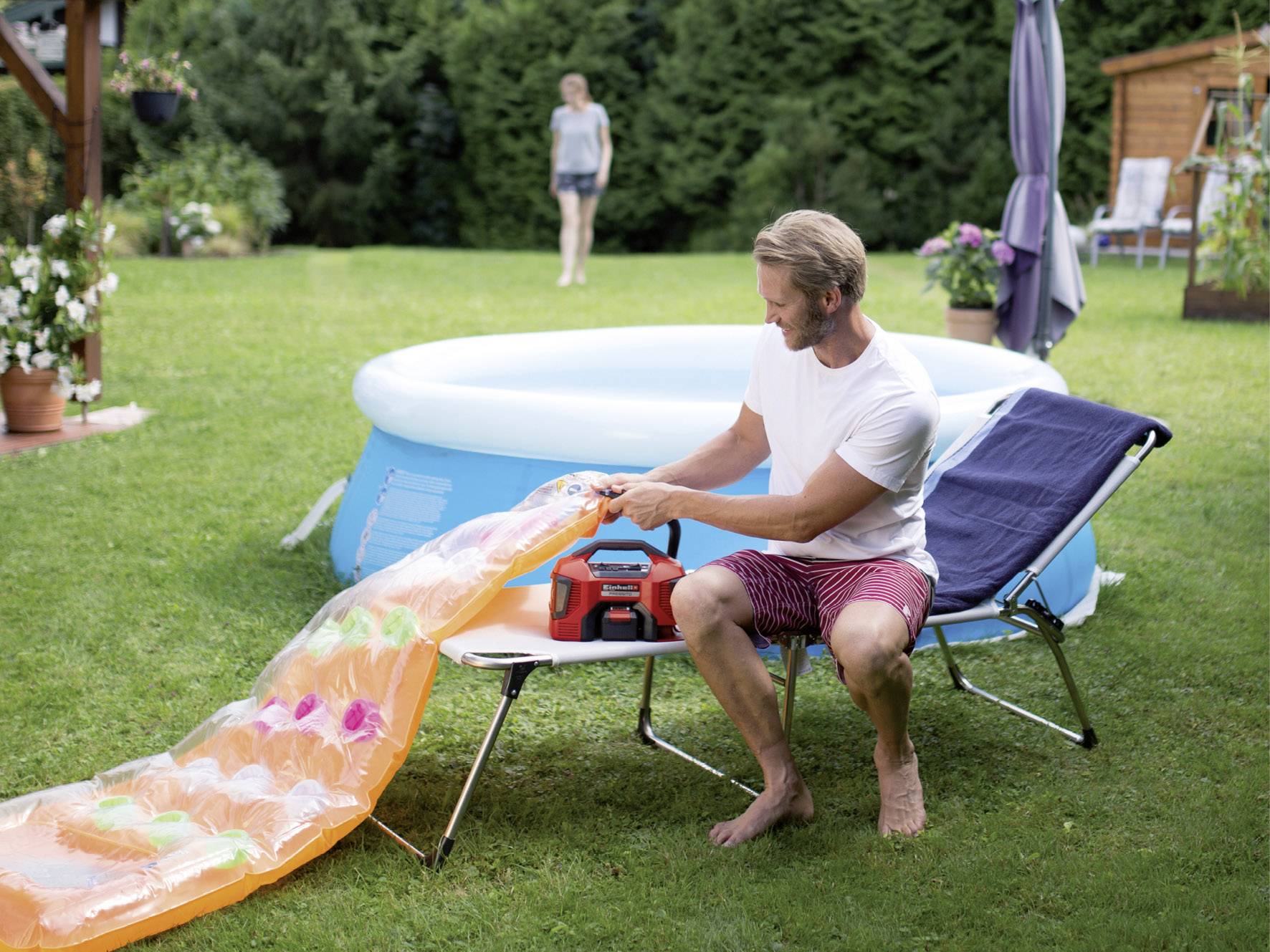 Mężczyzna pompuje materac dmuchany na leżaku w ogrodzie. W tle stoi basen dmuchany.