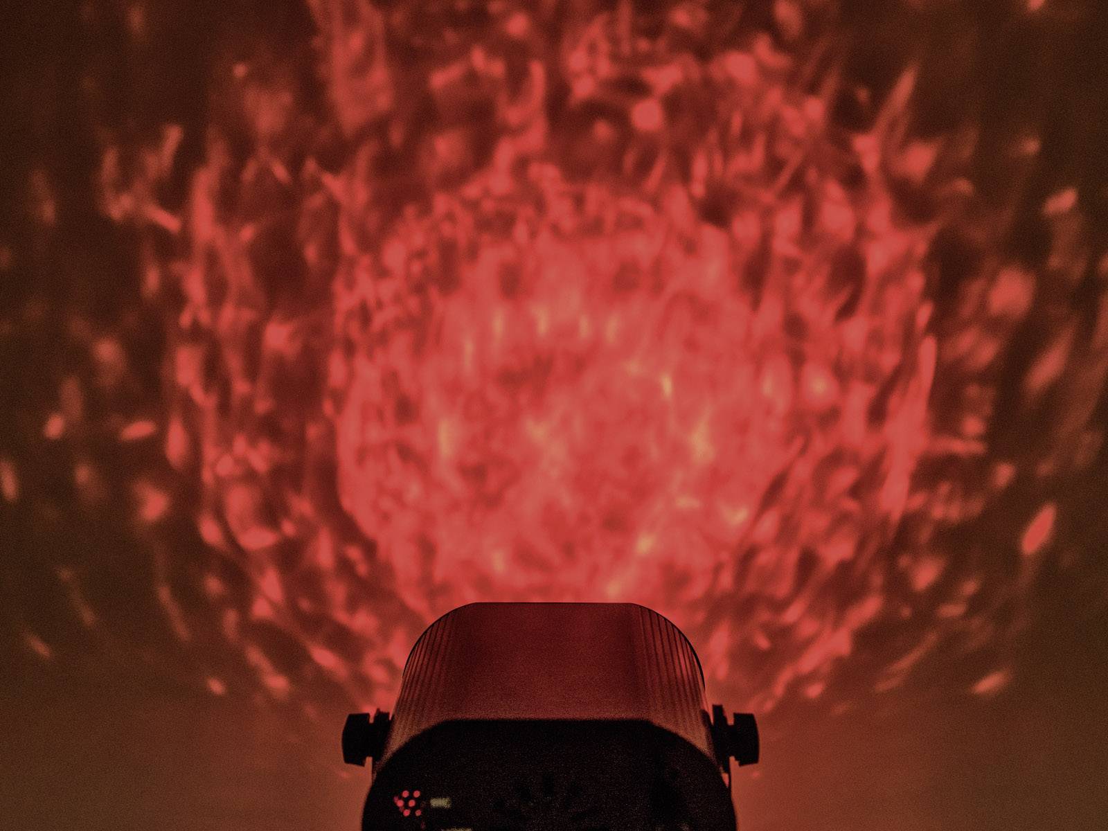 Efekt świetlny rzuca dynamiczne czerwone wzory na ścianę. Abstrakcyjne kształty generowane w tle wyglądają żywo i energicznie.