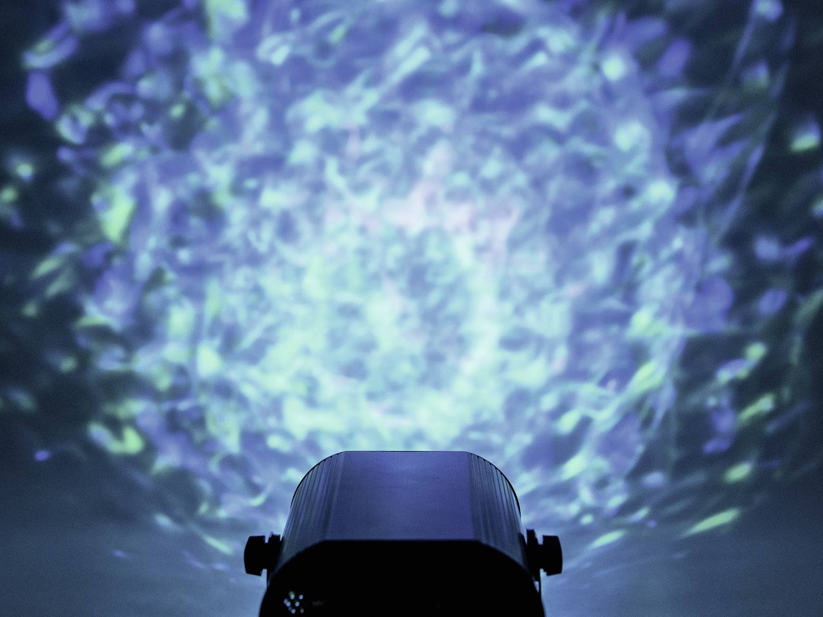 Projektor świetlny rzuca na ścianę niebieskie, faliste wzory przypominające odbicia wody.