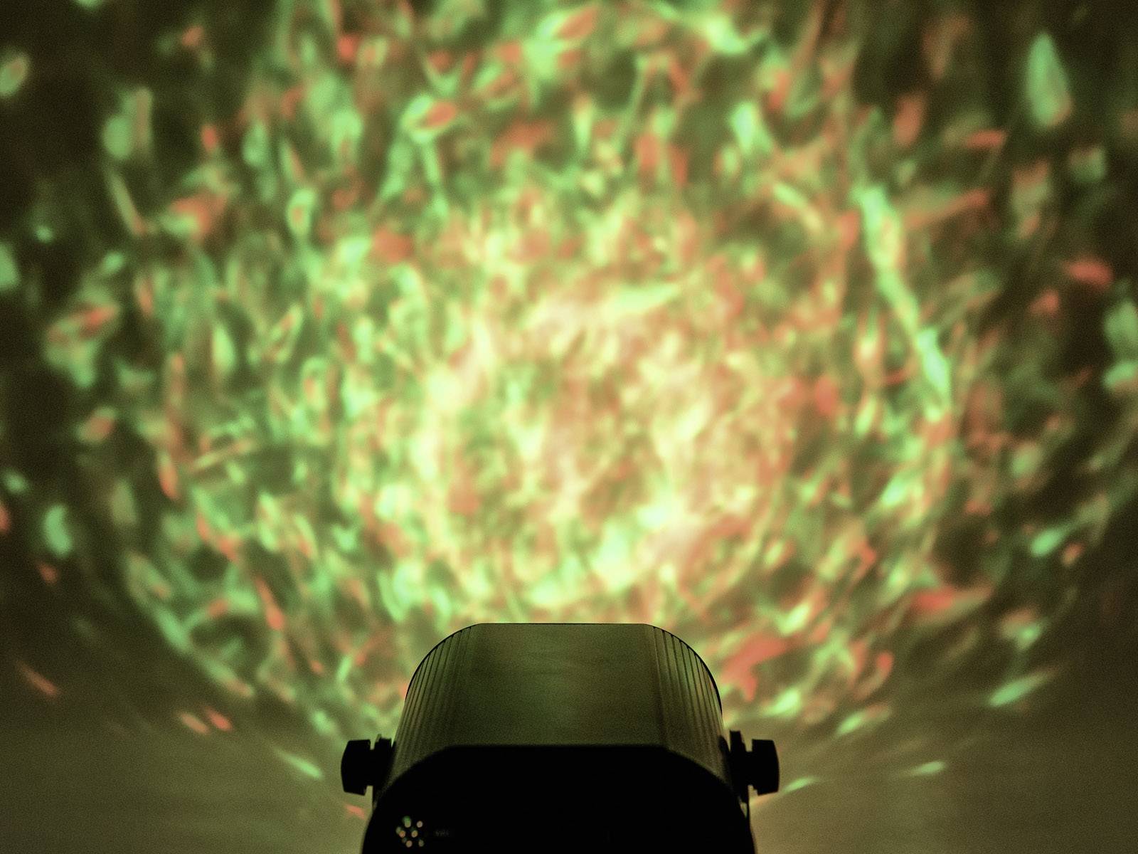 Projektor rzuca abstrakcyjny wzór w odcieniach zieleni i czerwieni na ścianę, tworząc efekt kalejdoskopowy.