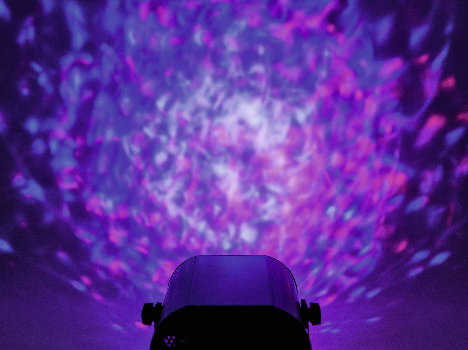 Projektor światła ultrafioletowego rzuca rozmazany, kalejdoskopowy wzór w odcieniach fioletu i błękitu na ścianę.