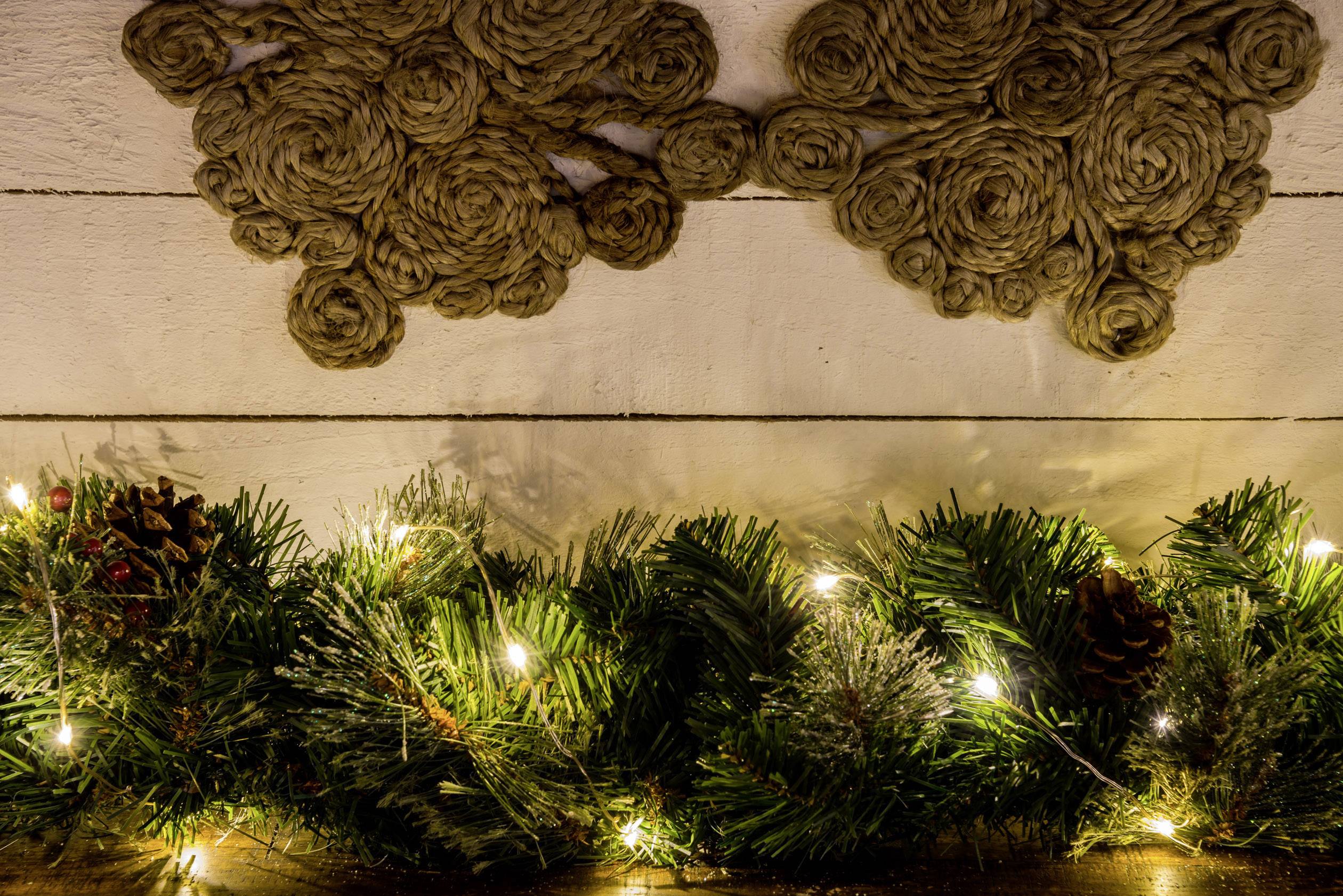 Świąteczny wieniec z zielonych gałązek i lśniących świateł wisi na ścianie, u góry ozdobionej skręconymi linami. Dekoracja bożonarodzeniowa.