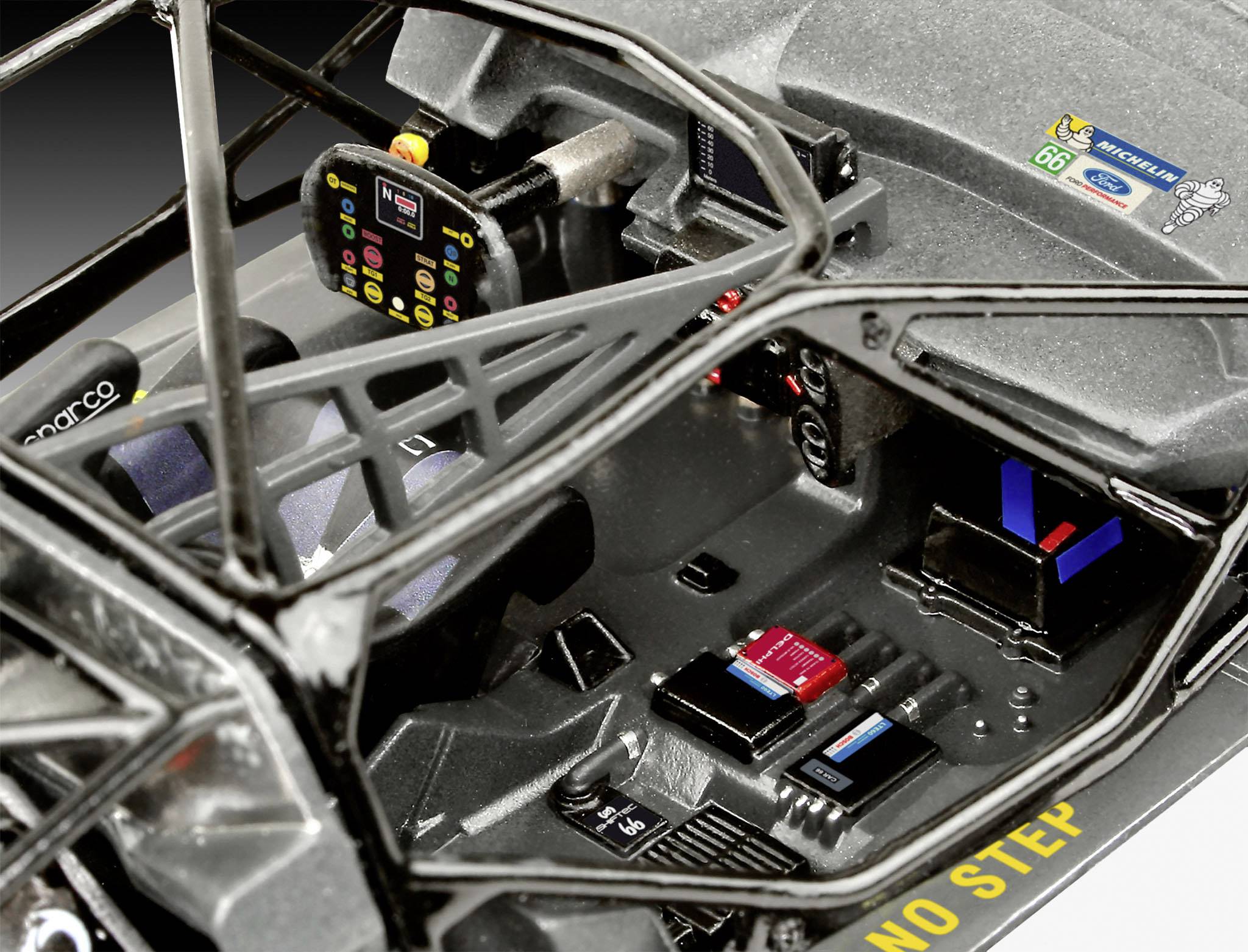 Wnętrze samochodu sportowego z czarną tapicerką i klatką bezpieczeństwa. Widoczny jest cyfrowy ekran i elementy sterujące.