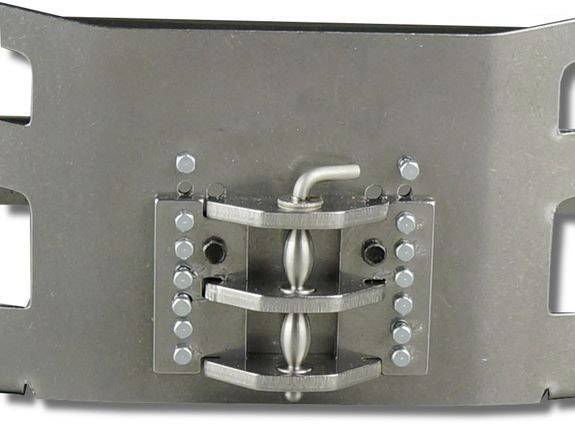 Mechanizm metalowy z centralnym korbowrotem i dwoma nakładającymi się na siebie elementami, otoczony śrubami, zamontowany na prostokątnej płycie.