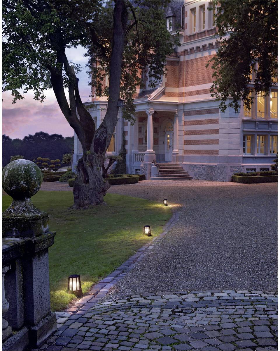 Oświetlona ścieżka prowadzi do dużego, eleganckiego budynku o zmierzchu. Latarnie uliczne oświetlają drogę, po lewej stronie stoi duże drzewo.