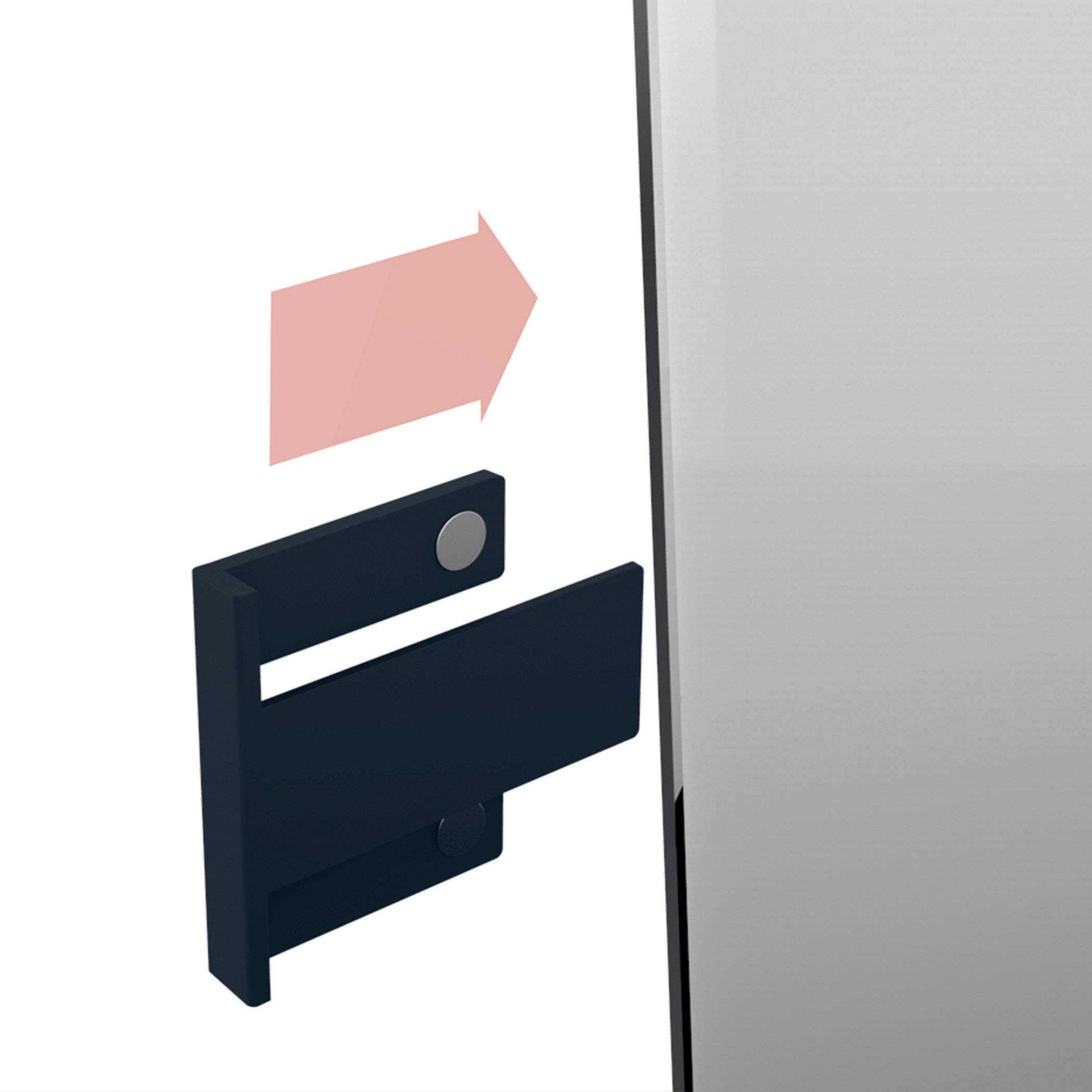 Czarny hak z magnesem zostaje przymocowany do boku metalowego obiektu. Czerwona strzałka wskazuje kierunek.