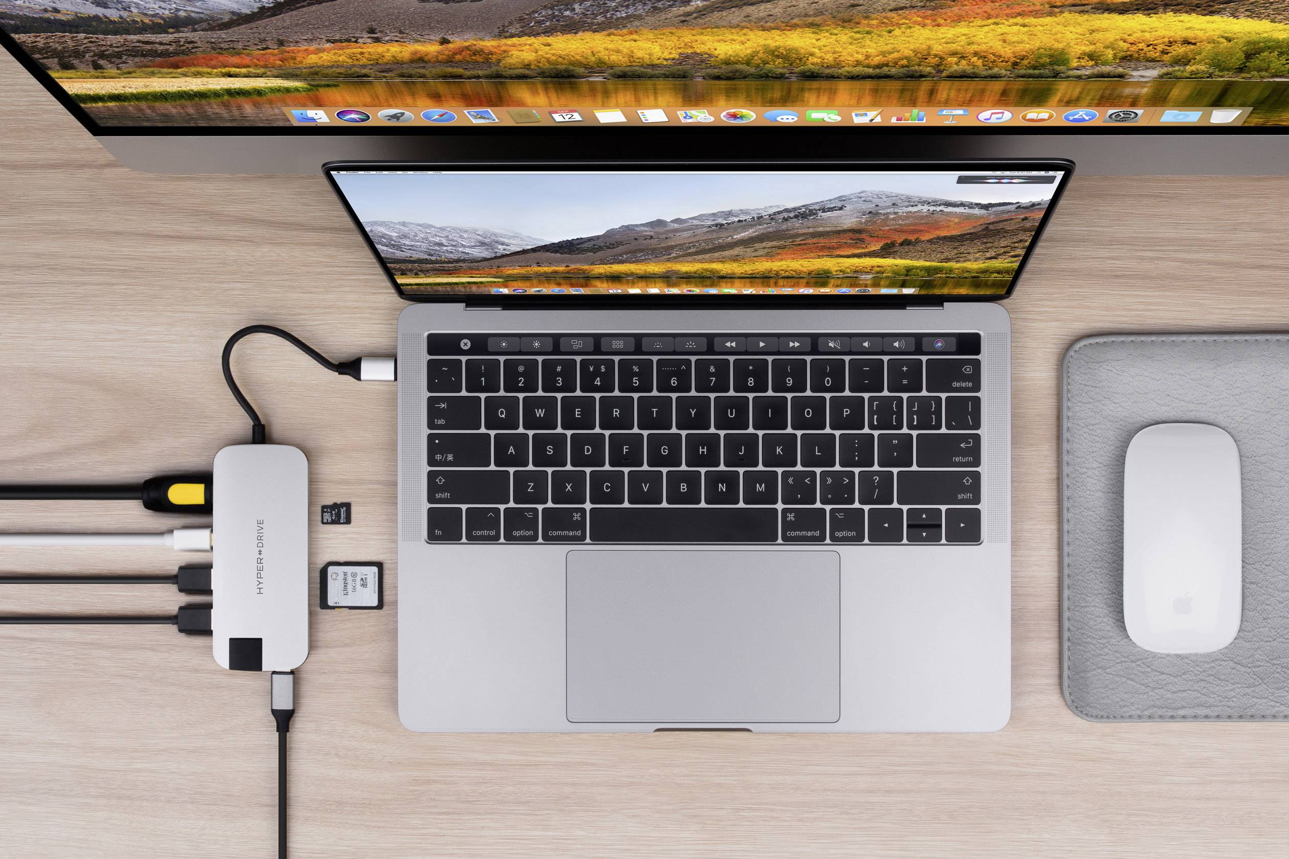 Laptop stoi na biurku, podłączony do kilku urządzeń za pośrednictwem koncentratora USB-C. Obok niego leży mysz.