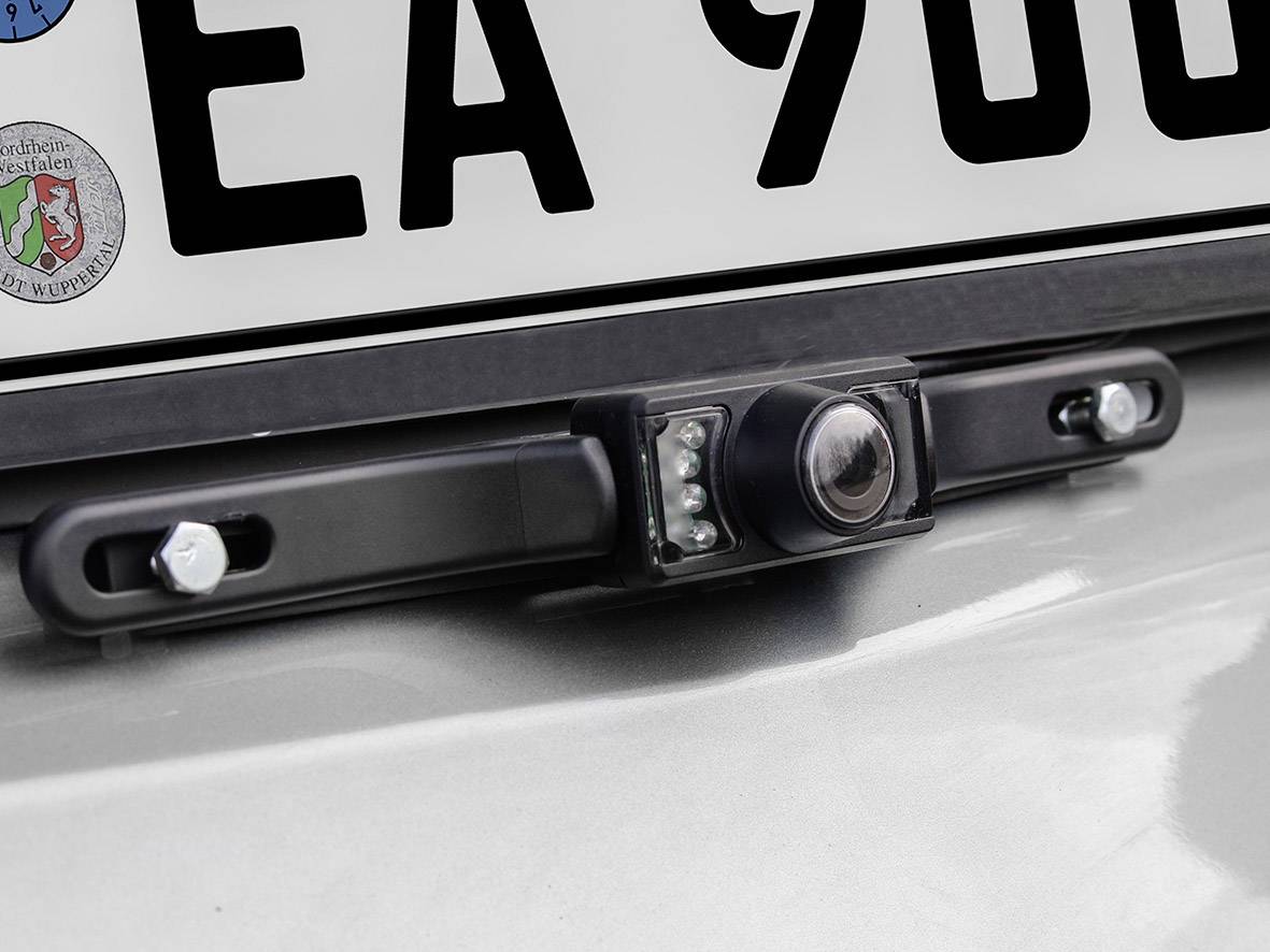 Kamera cofania zamontowana pod tablicą rejestracyjną samochodu. Urządzenie posiada kilka małych diod LED wokół obiektywu.