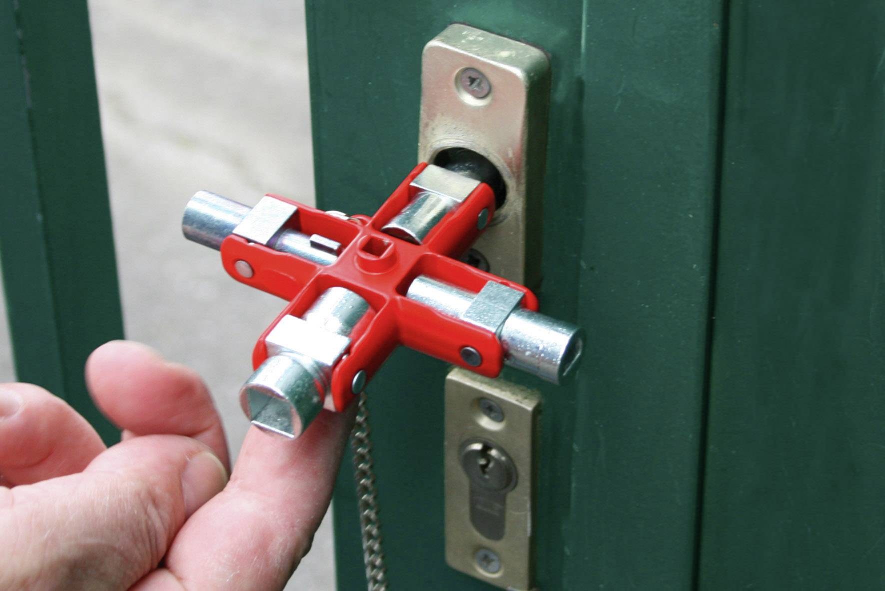 Dłoń trzyma czerwony klucz czterokątny w zamku drzwiowym, demonstrując bezpieczeństwo lub dostęp.