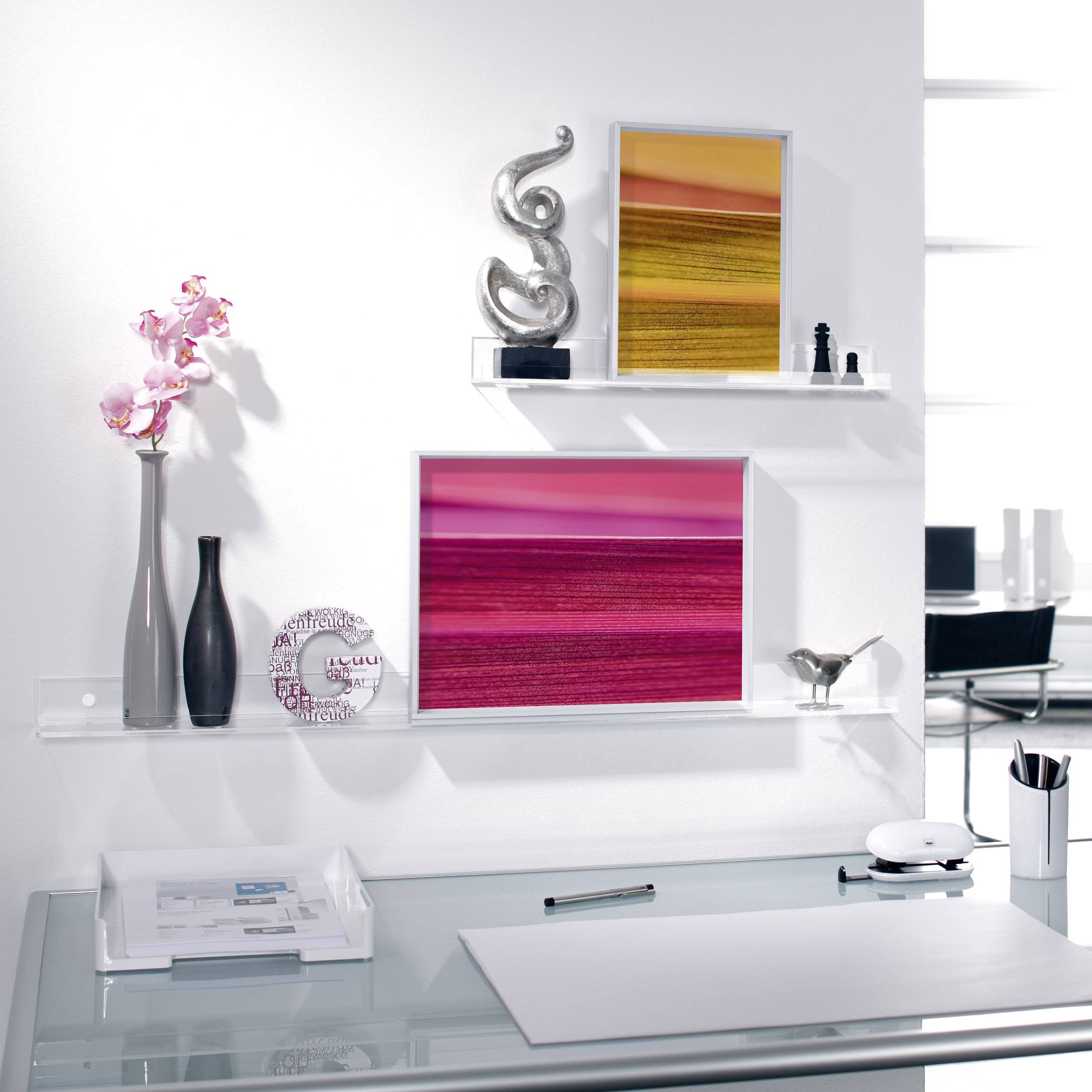 Nowoczesne biurko ze szklaną powierzchnią, ozdobione białymi i czarnymi wazonami, różowymi dziełami sztuki oraz orchideą.