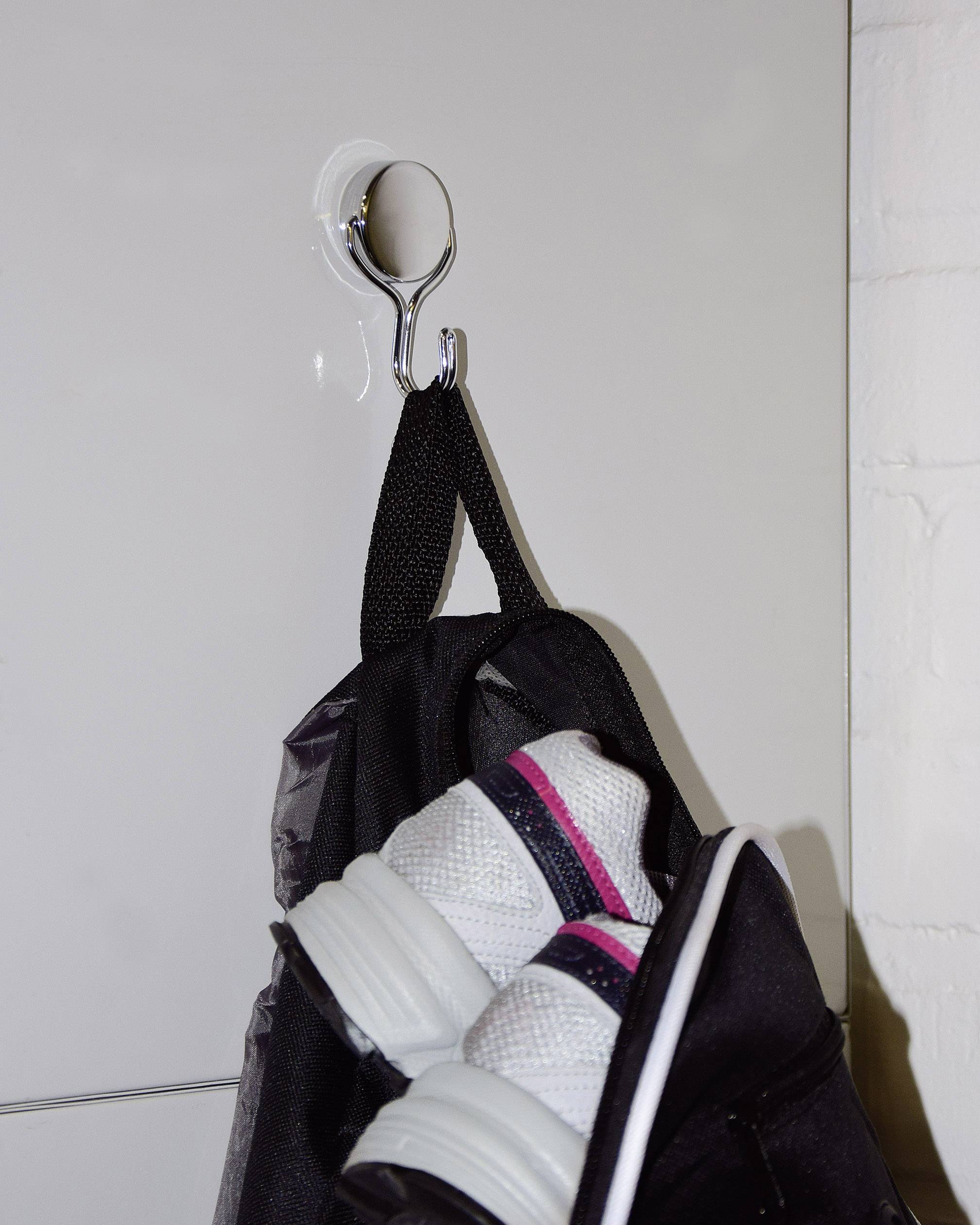 Czarny plecak wisi na haku. Z plecaka wystają białe buty sportowe z różowymi paskami.