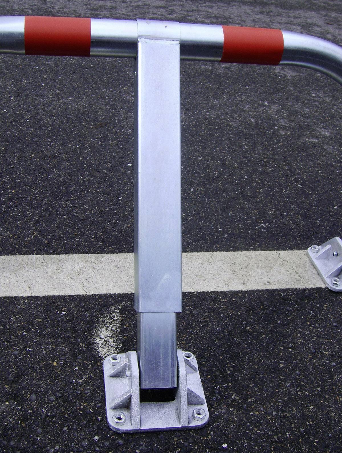 Metalowa bariera na asfaltowej nawierzchni, oznaczona czerwonymi paskami, służy do wyznaczenia i ograniczenia określonego obszaru.