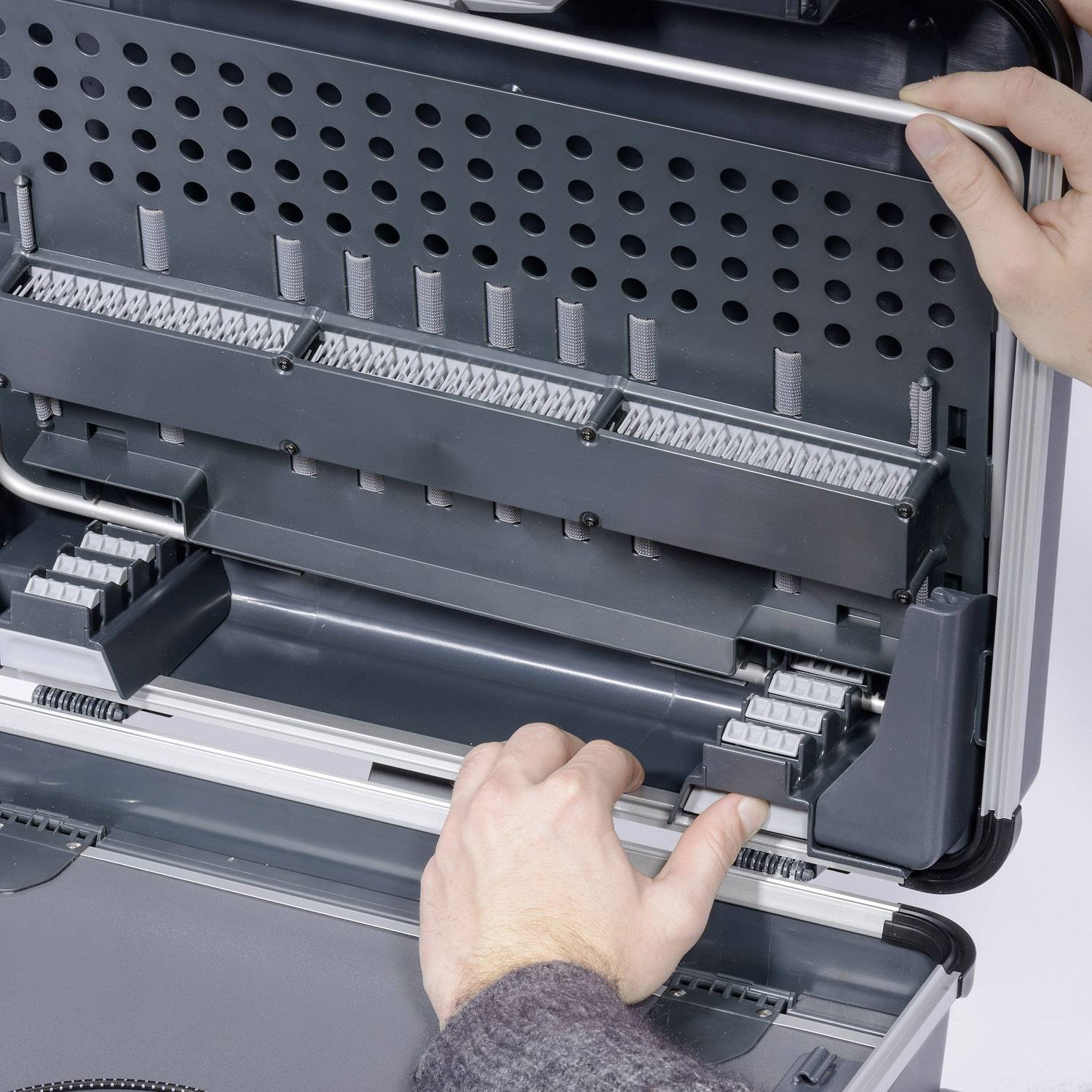 Osoba otwiera szary kufer na narzędzia z różnymi przegródkami i uchwytami, służący do organizacji narzędzi.