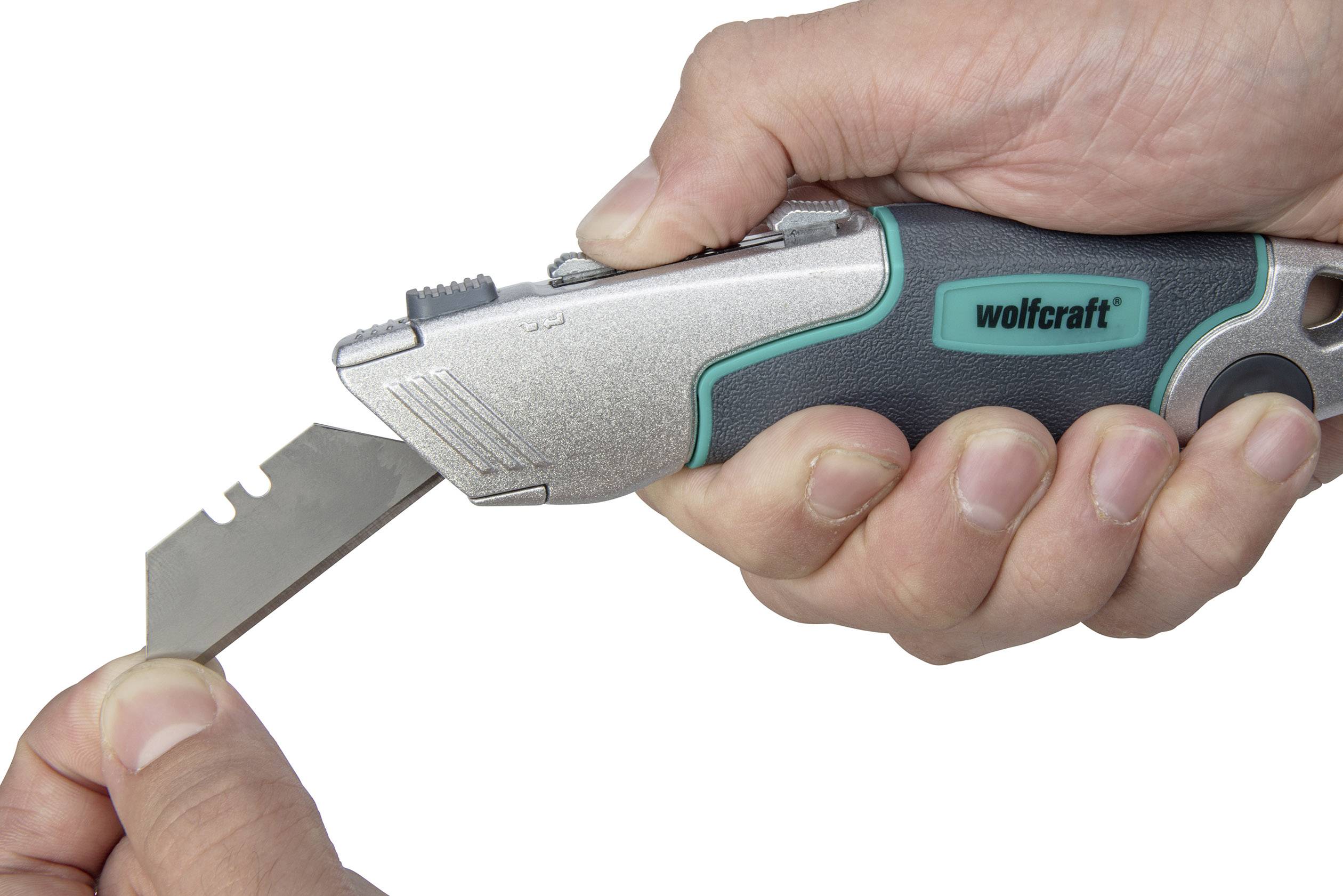 Osoba trzyma uniwersalny nóż Wolfcraft i wymienia ostrze drugą ręką.