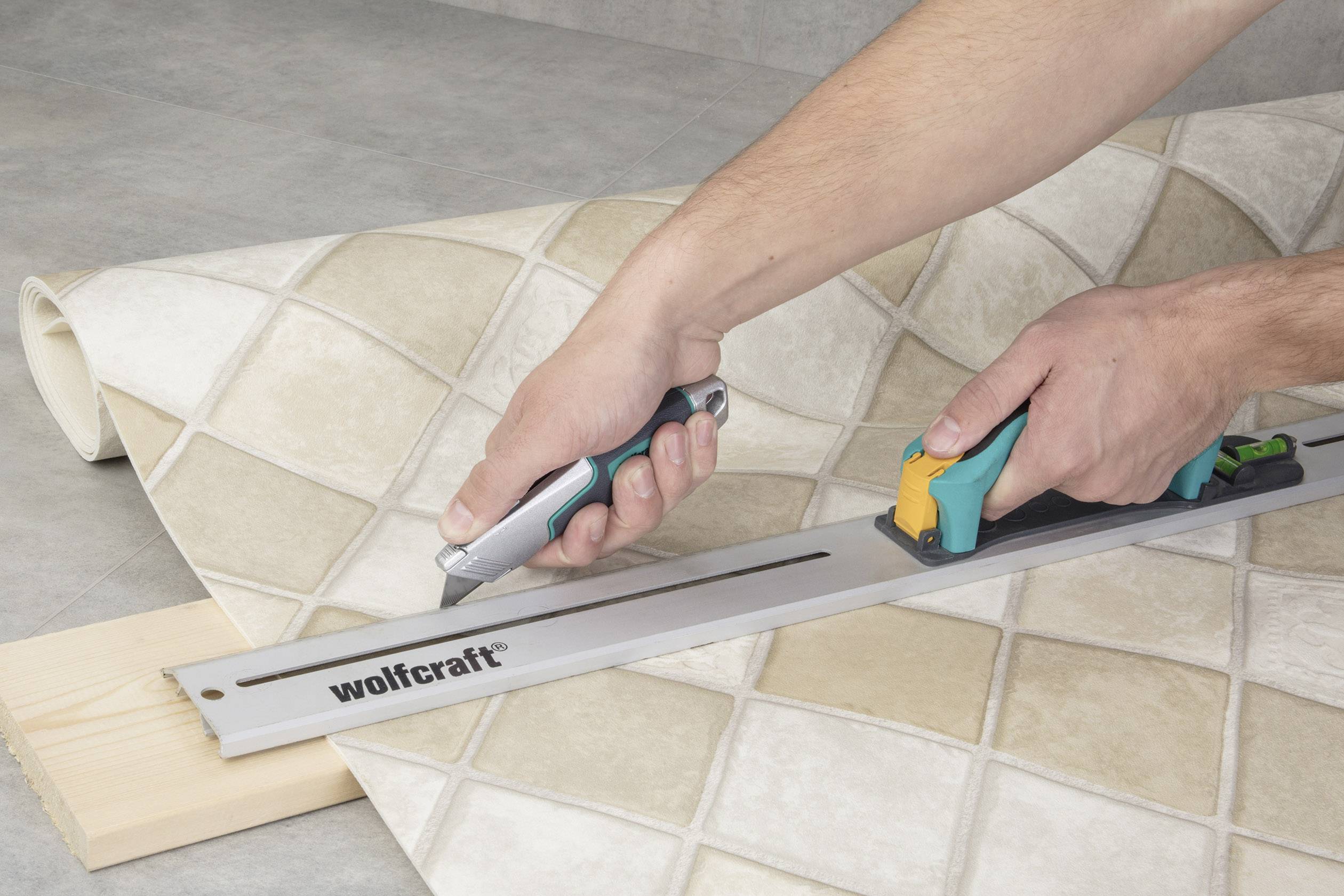 Dwie ręce wycinają za pomocą noża i szyny prowadzącej płytki podłogowe z jasnego materiału.