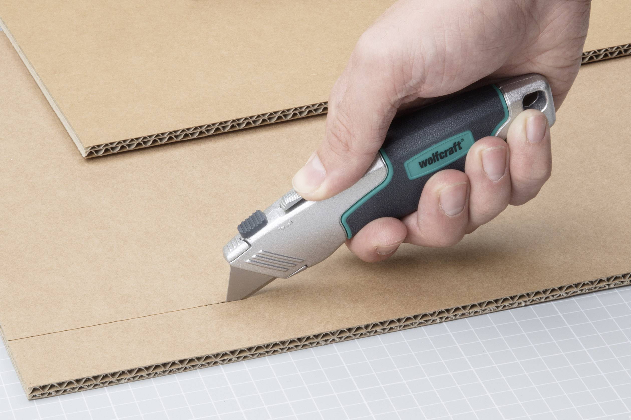 Ręka tnie nożem introligatorskim arkusz tektury falistej na macie do cięcia.