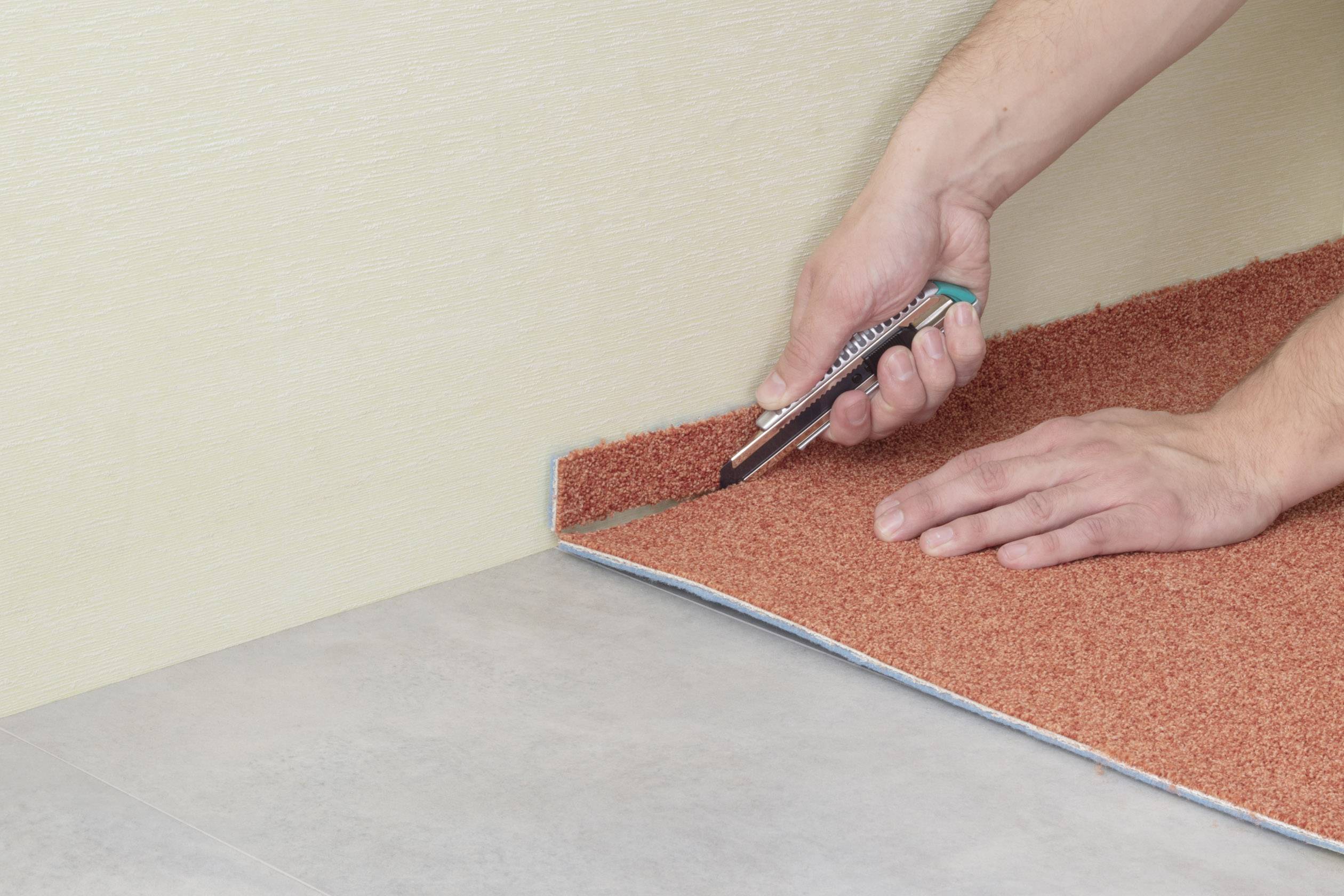 Dywan jest przycinany wzdłuż ściany nożem do dywanów, aby dopasować go do odpowiedniego rozmiaru.