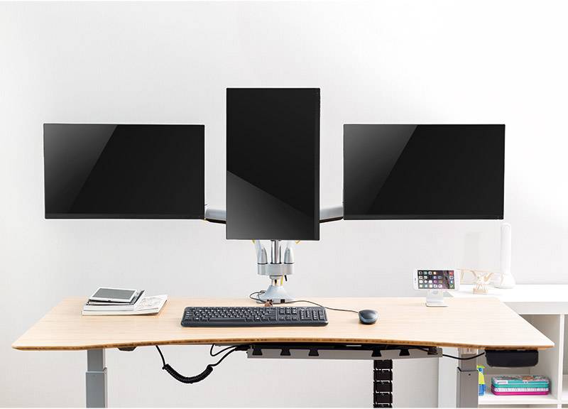 Trzy monitory komputerowe na biurku z regulacją wysokości. Środkowy monitor jest ustawiony pionowo. Poniżej klawiatura.