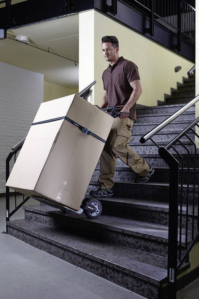 Mężczyzna transportuje duży karton po schodach za pomocą wózka transportowego do przewozu towarów.