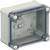 Szary, przezroczysty obudowa puszka, prostokątna, z śrubami w narożnikach, odpowiednia do instalacji elektrycznych.