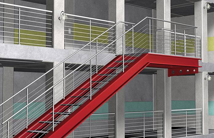 Czerwona balustrada schodowa w nowoczesnym wielopiętrowym budynku, otoczona szarymi ścianami betonowymi z kolorowymi panelami.