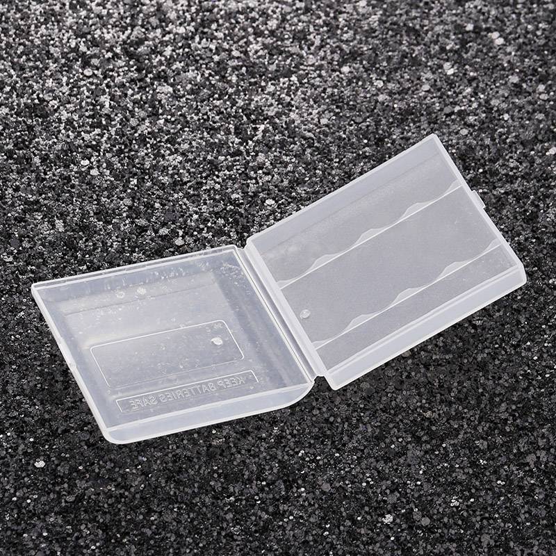 Przezroczysta, pusta plastikowa obudowa na czarnym, ziarnistym tle, otwarta, z miejscem na cztery baterie AA.