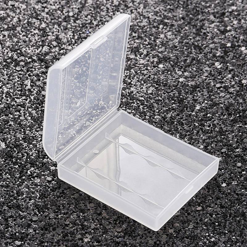 Przezroczyste plastikowe pudełko z otwartą pokrywką stoi na ciemnej, teksturowanej powierzchni. Pudełko jest puste.