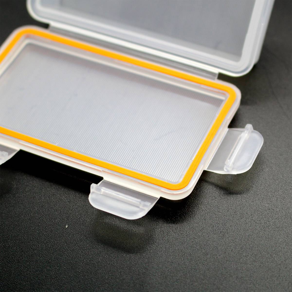 Biała, otwierana plastikowa skrzynka z pomarańczową krawędzią, umieszczona na czarnym podłożu.