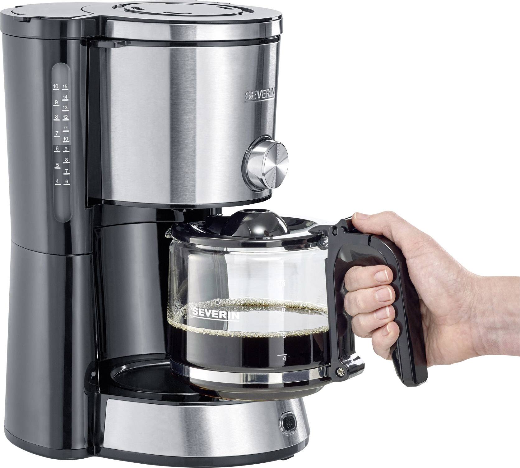 Jedna ręka trzyma szklaną dzbanek z świeżo zaparzoną kawą, która spływa z srebrnego ekspresu do kawy.