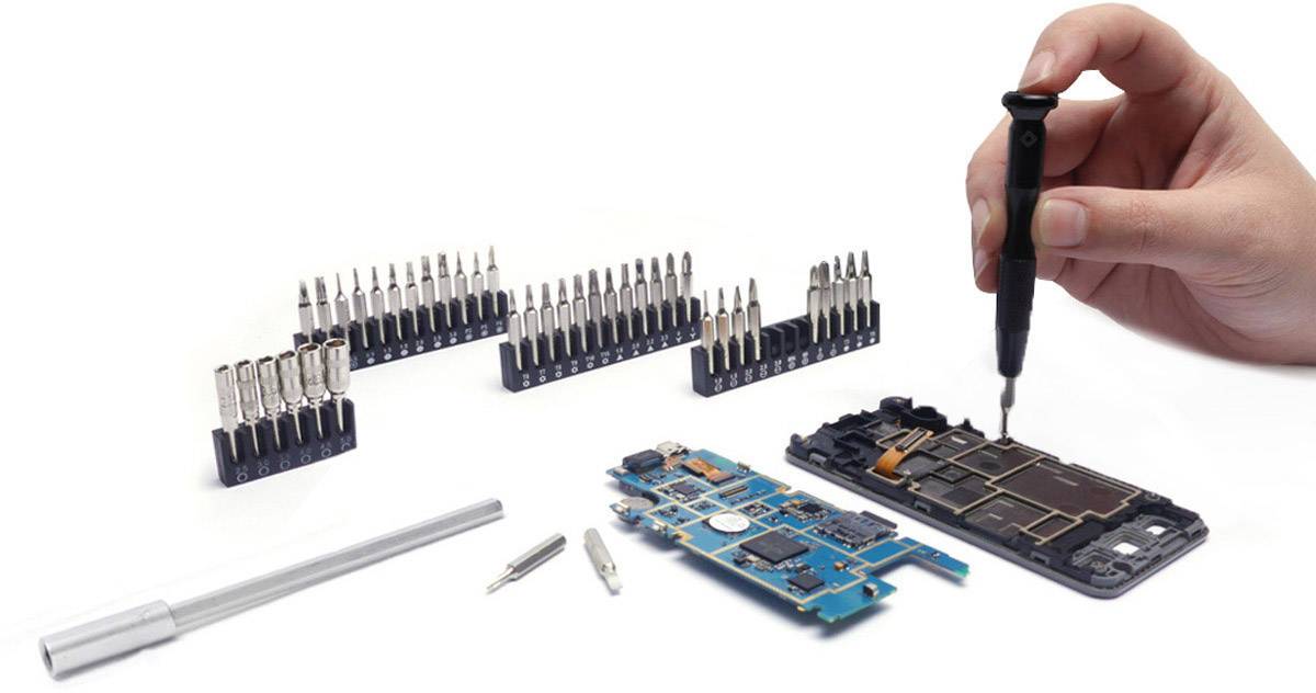 Dłoń naprawia smartfona za pomocą śrubokręta. Na pierwszym planie leżą narzędzia i części.