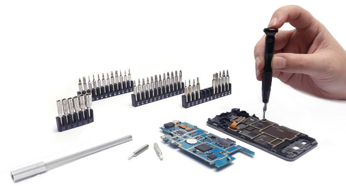 Ręka montuje smartfon wkrętakiem, otoczona narzędziami i częściami zamiennymi.