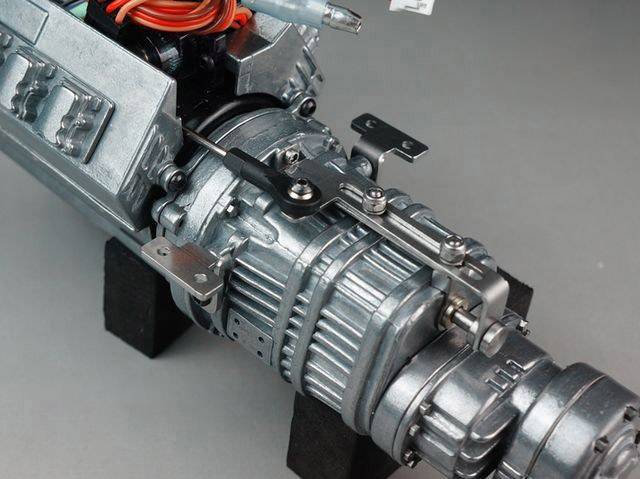 Zbliżenie silnika maszynowego z widocznymi metalowymi elementami i przewodami. Silnik jest zamontowany na czarnych mocowaniach.