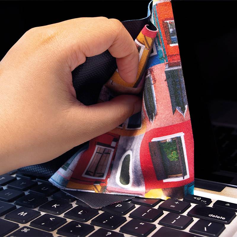 Dłoń przesuwa kolorową ściereczką po klawiaturze laptopa.