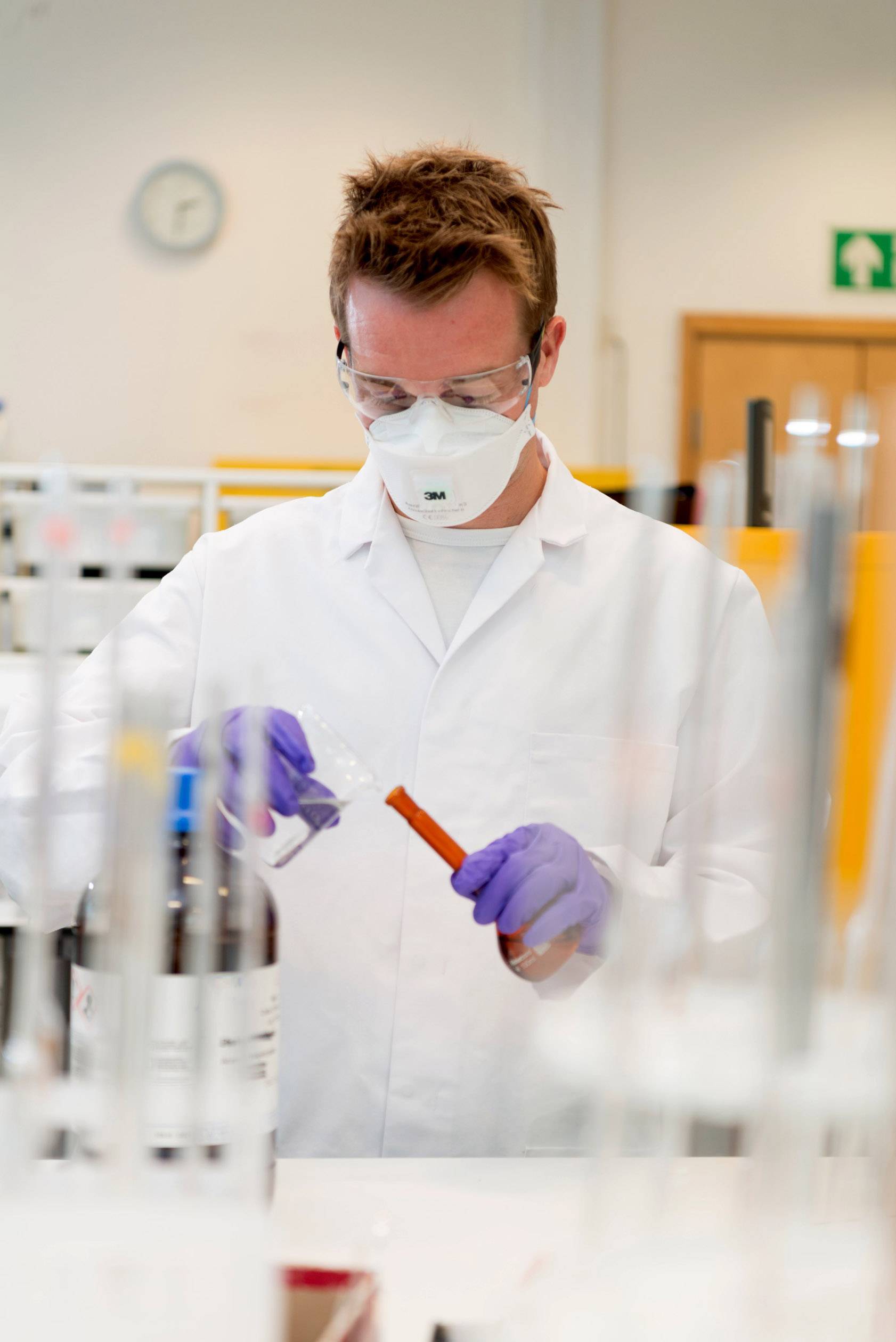 Naukowiec w białym kitlu laboratoryjnym przeprowadza eksperymenty z probówką, ubrany w okulary ochronne i rękawiczki.