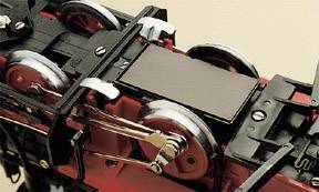 Zabawkowa lokomotywa sfotografowana od dołu, z fokusem na kołach i metalowych elementach.