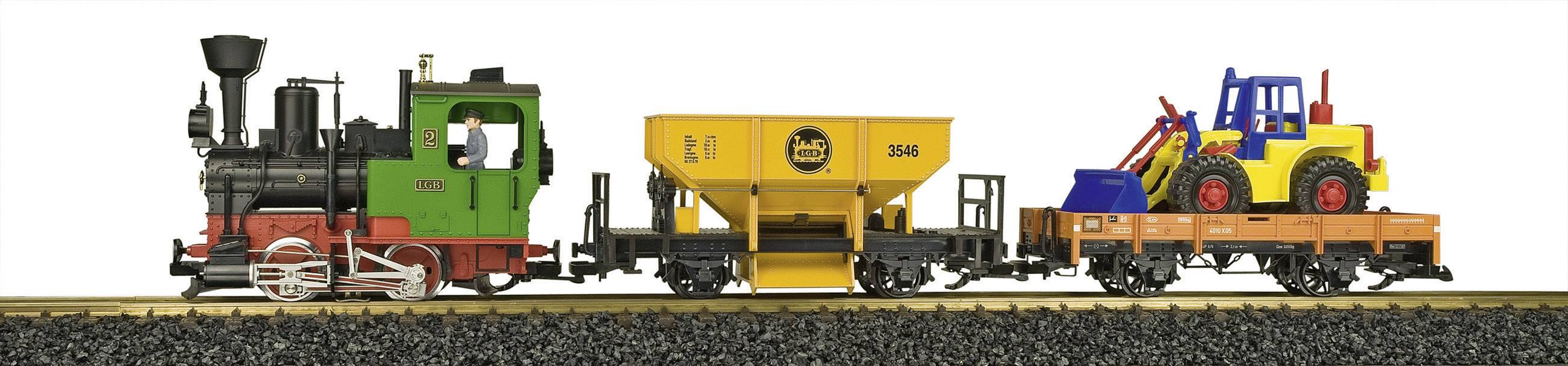 Zabawkowa kolej z zieloną lokomotywą, żółtym wagonem wywrotką i pomarańczowym wagonem platformą, załadowanym niebiesko-czerwonym traktorem na torach.