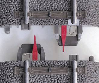 Zbliżenie dwóch brązowych szyn kolejki modelowej z czerwonymi dźwigniami sterowania zwrotnicami na szarym podłożu.