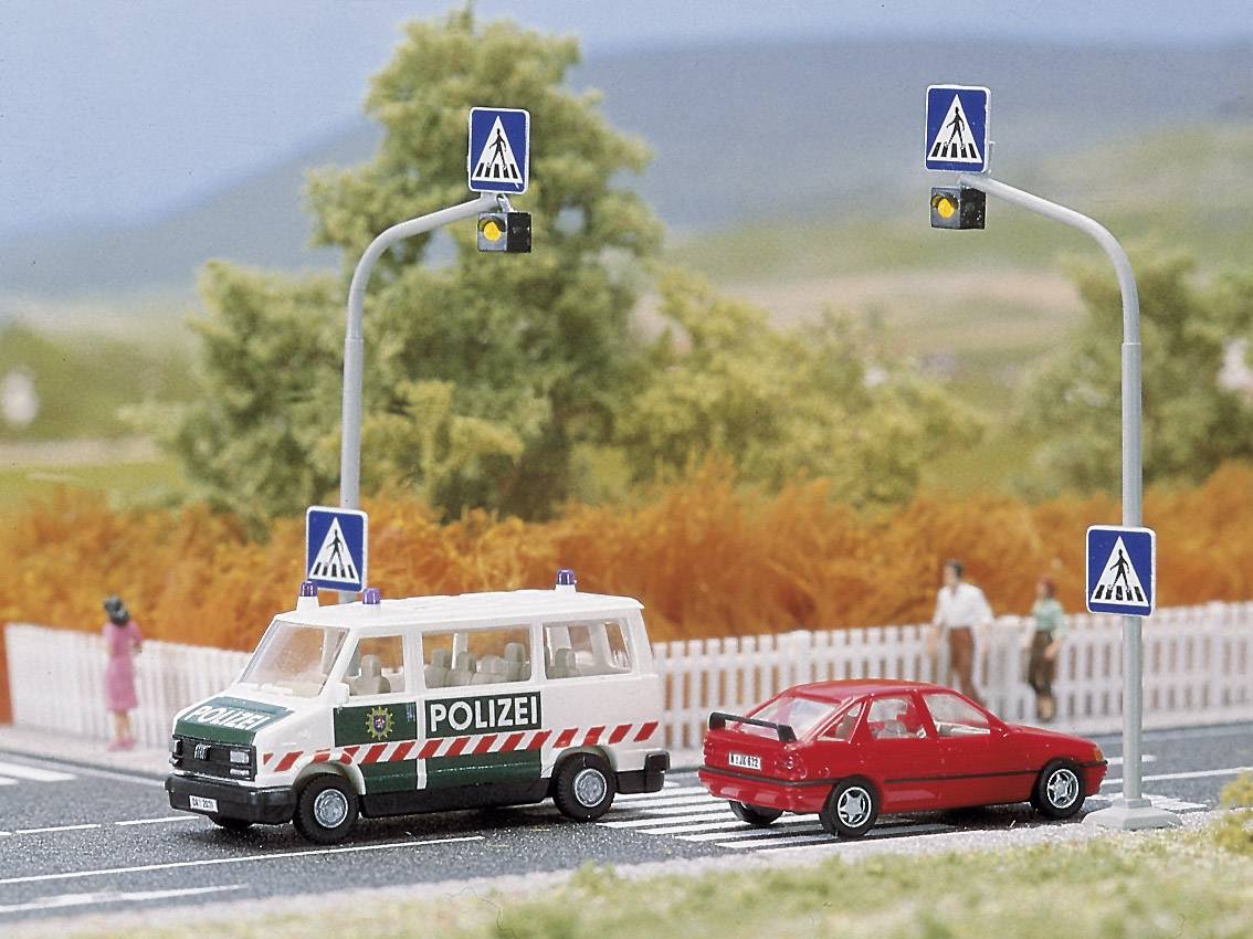 Czerwony samochód i radiowóz stoją na przejściu dla pieszych w miniaturowej scenie. Ludzie czekają przy krawędzi ulicy.