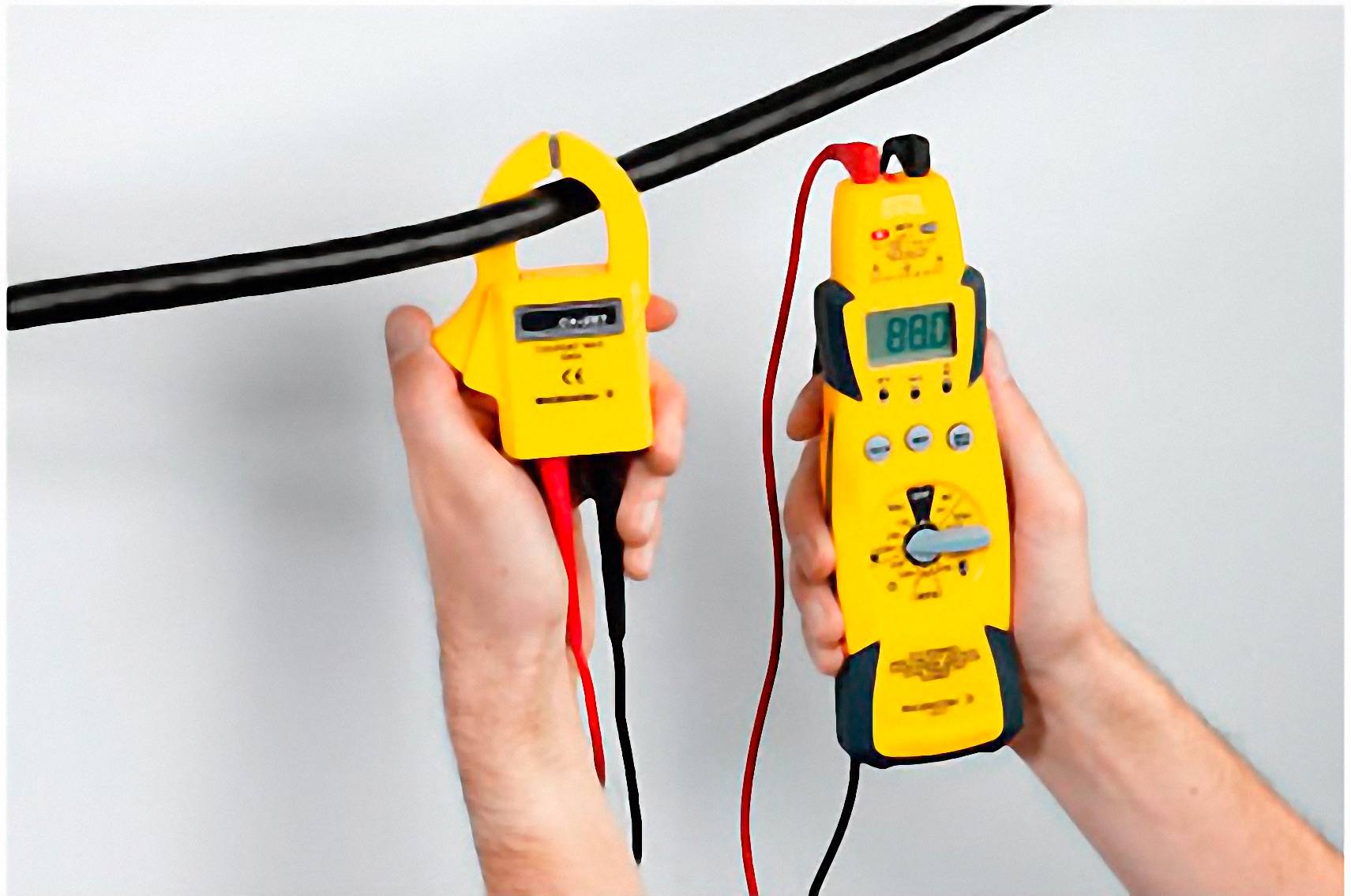Osoba trzyma żółty miernik prądu oraz szczypce, badając przewód elektryczny. Wyświetlacz urządzenia pokazuje cyfrowy pomiar.