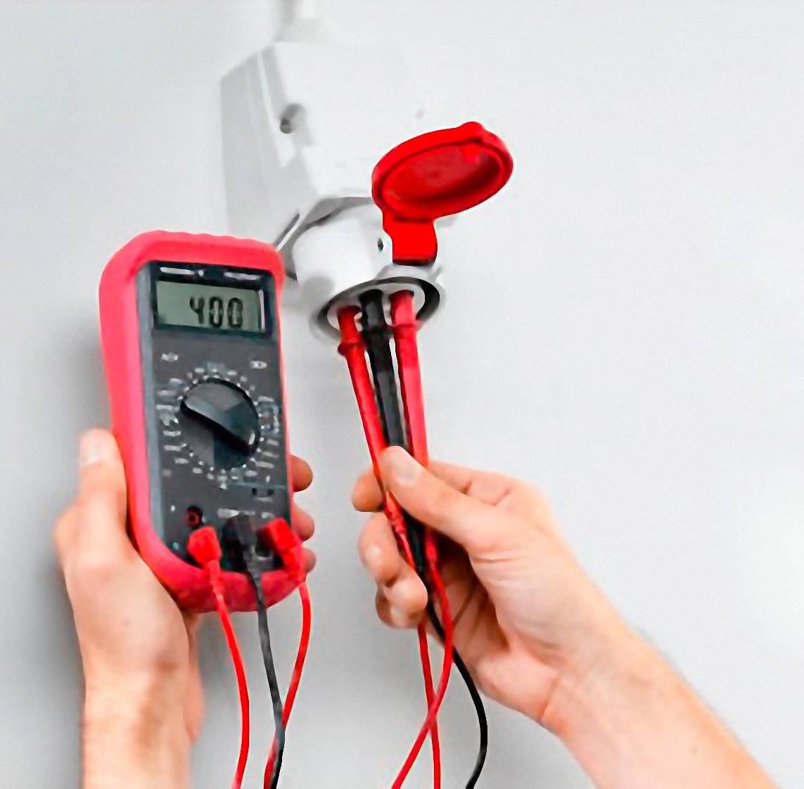Osoba mierzy napięcie w gniazdku elektrycznym za pomocą multimetru. Wyświetlacz wskazuje 240 woltów.