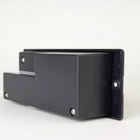 Prostokątna, czarna metalowa obudowa z czterema widocznymi śrubami w rogach, leżąca na jasnej powierzchni.