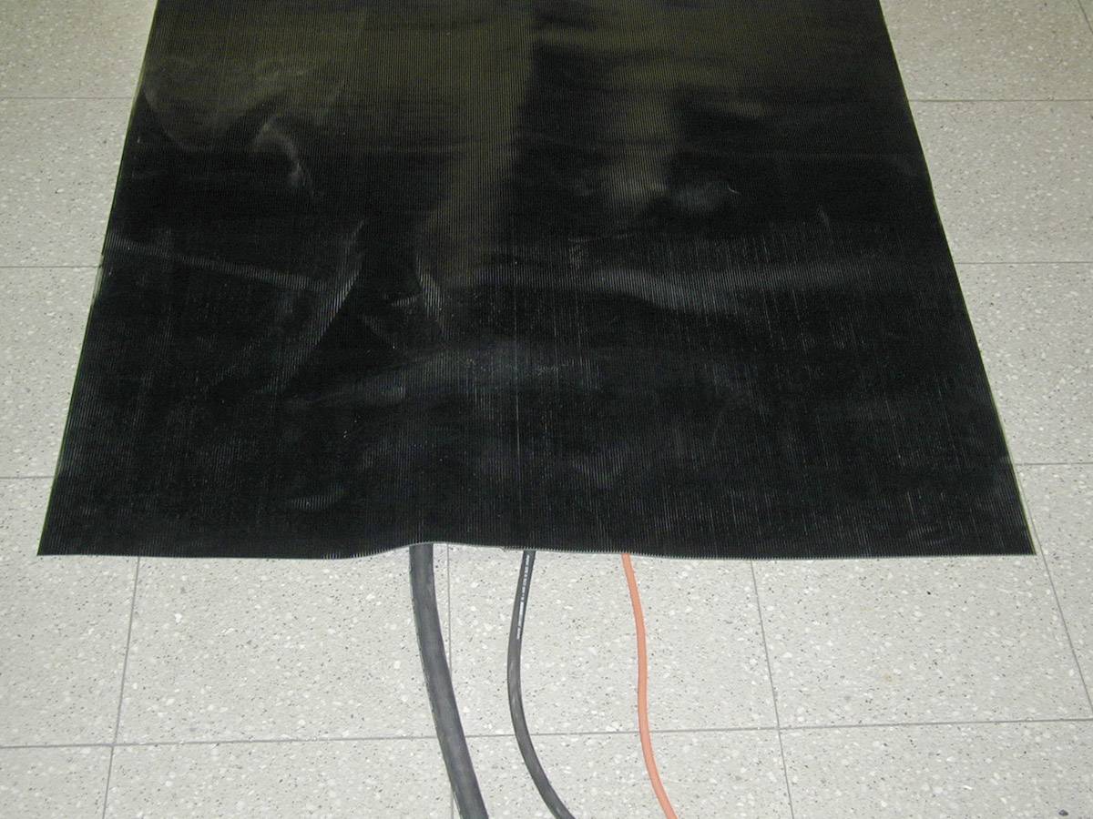 Duży, czarny prostokąt z kablami pod spodem na szarej podłodze z płytek.