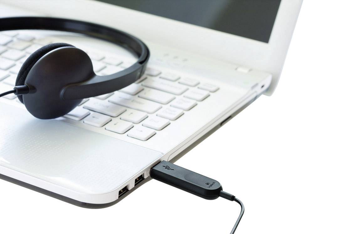 Czarne słuchawki leżą na klawiaturze białego laptopa, który jest podłączony przez pendrive'a po prawej stronie.